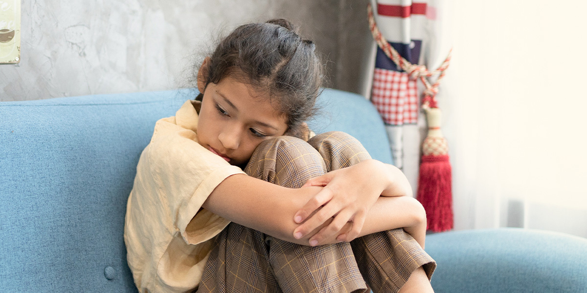 Child hugging her knees sitting down